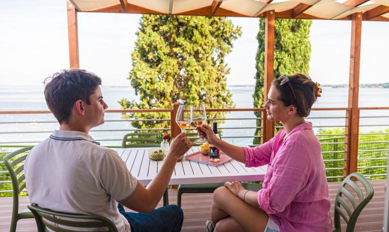 Zwei Personen stoßen auf einer Terrasse mit Meerblick an.