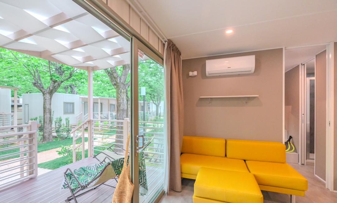 Modern mobile home with yellow lounge and outdoor veranda.