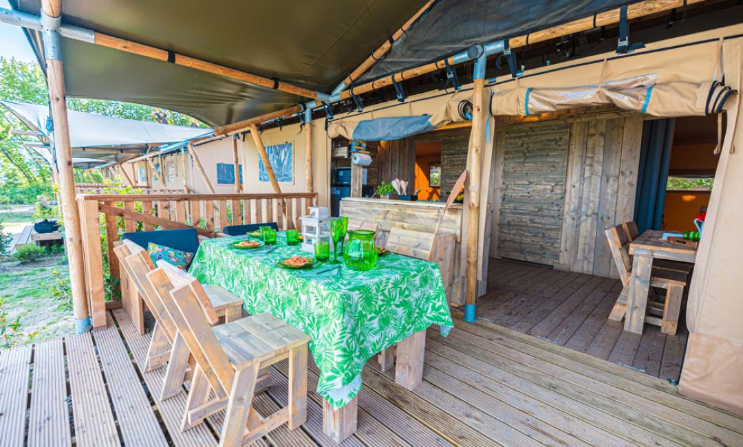 Area pranzo all'aperto con tavolo verde, sedie in legno e ambiente naturale.