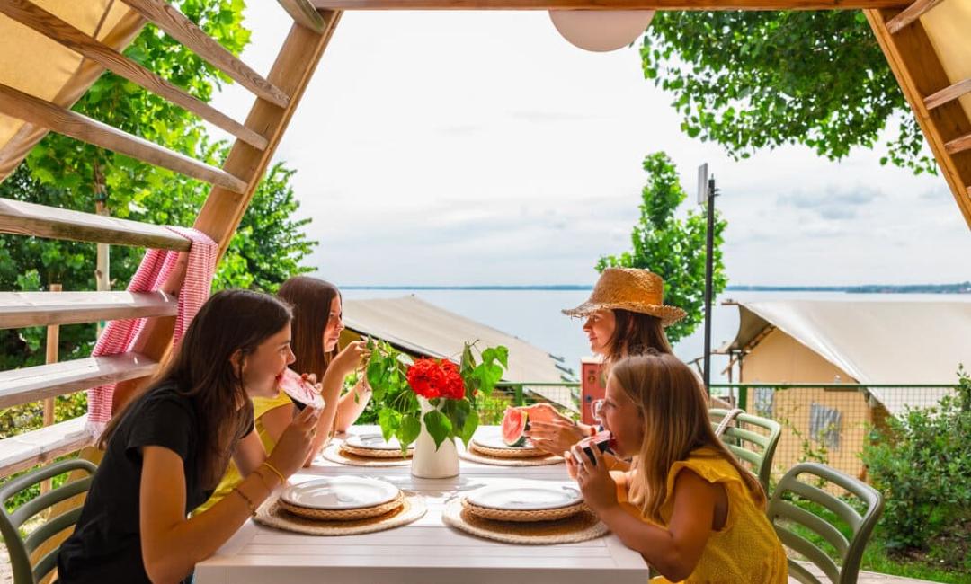 Four people eating watermelon on a veranda with lake view.