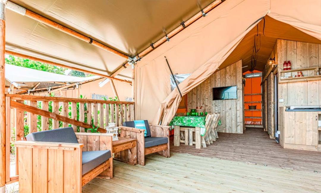 Tenda glamping con arredi in legno, zona relax e cucina attrezzata.