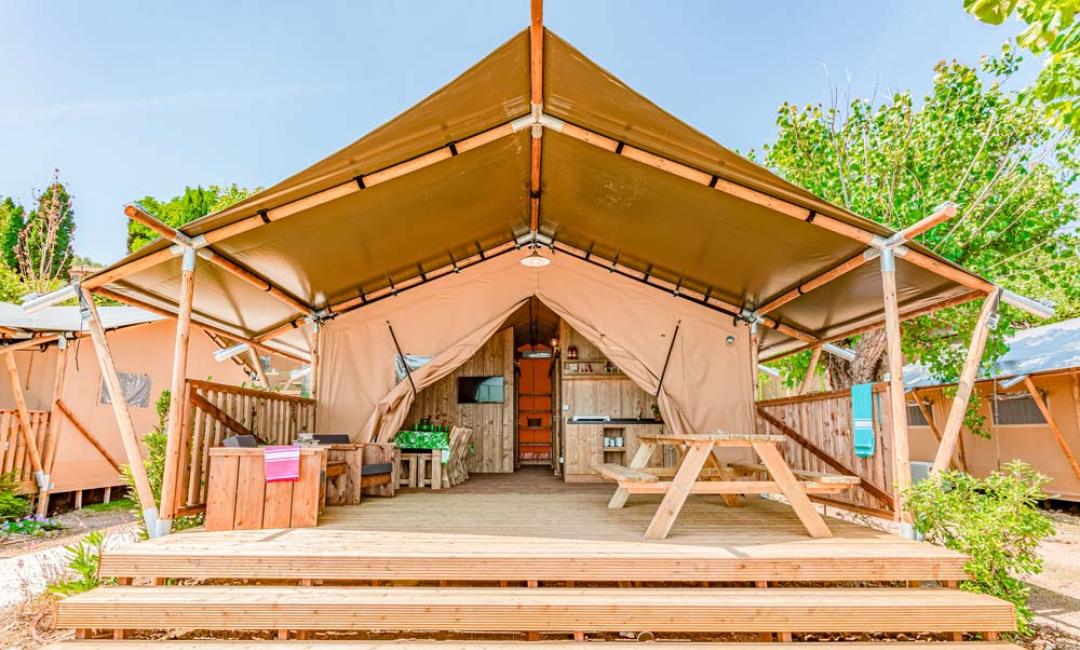 Tenda glamping con veranda e tavolo da picnic in un ambiente naturale.