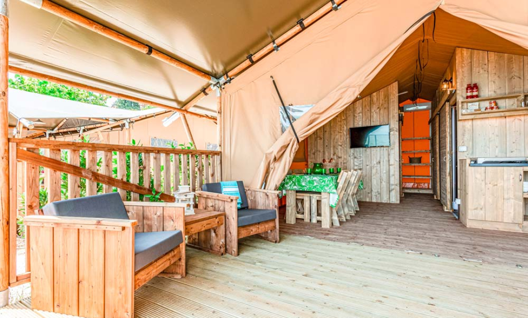 Tente glamping avec mobilier en bois et espace de vie extérieur.