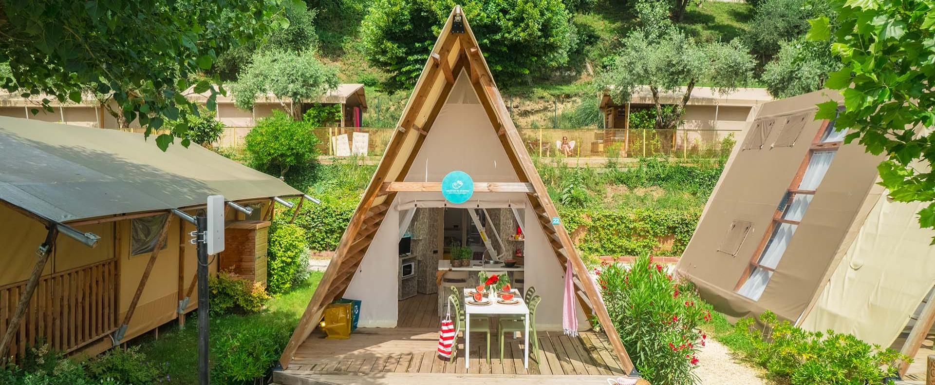 Tenda glamping in mezzo alla natura con veranda e tavolo apparecchiato.