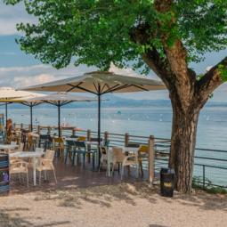 Restaurant im Freien mit Seeblick, Sonnenschirmen und Tischen.