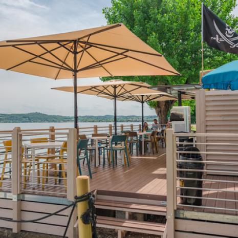 Terrasse am See mit Sonnenschirmen, bunten Tischen und Stühlen.