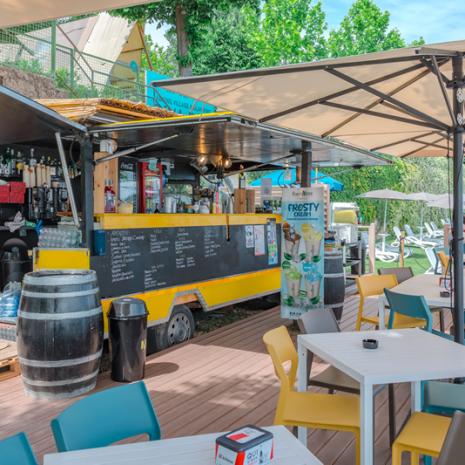 Freiluftkiosk mit bunten Tischen und Stühlen, umgeben von Sonnenschirmen.